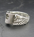 Silver ring with wing design and screw detail on a dark surface.