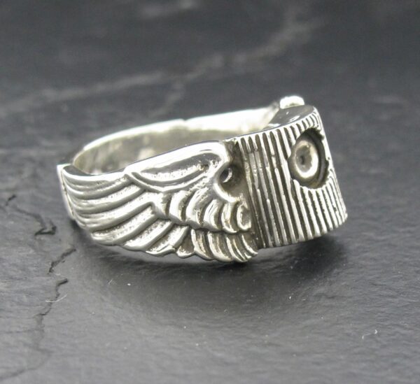 Close-up of a silver owl-themed ring with detailed wings on a dark surface.