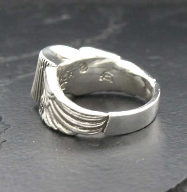 Close-up of a silver ring with wing-like engravings.