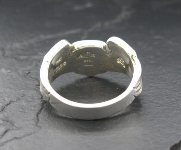 Close-up of a silver ring with an open design on a dark surface.