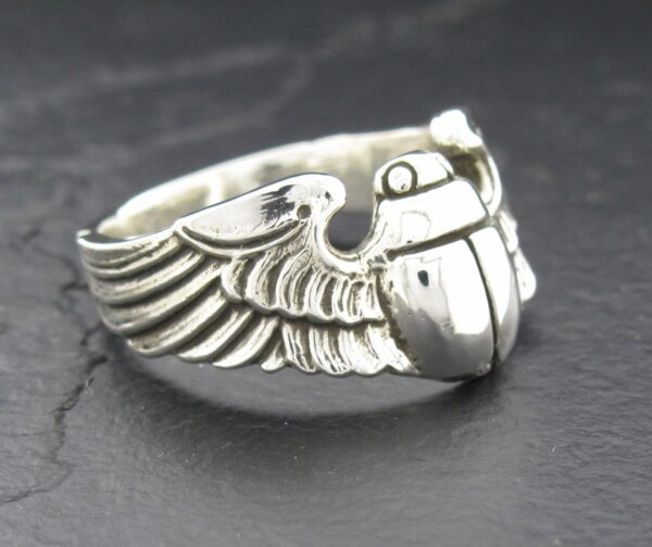 Close-up of a silver ring with detailed wing and grenade design.