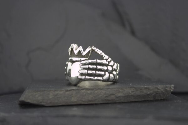 Silver skeleton hand ring with a crown design on top.