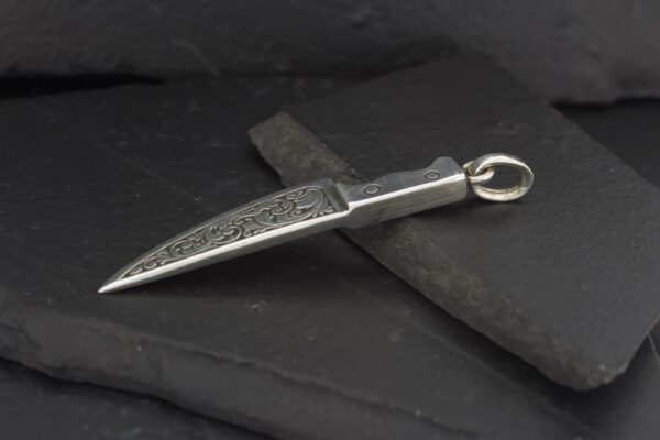 A detailed silver dagger pendant on a dark surface.