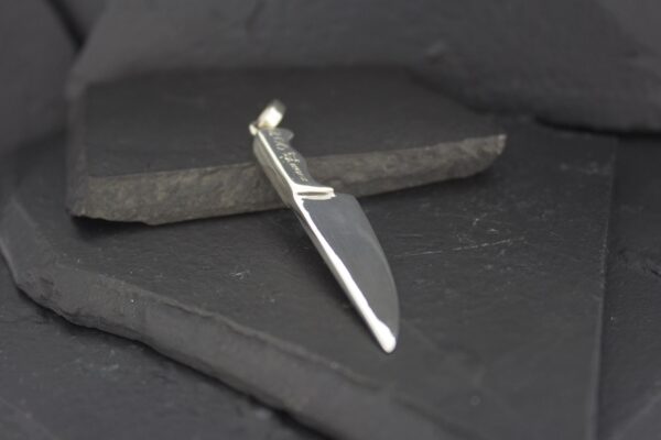 A silver knife pendant on a dark slate surface.