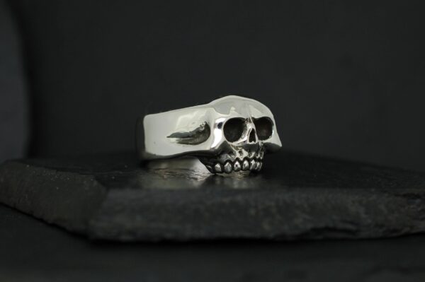 Silver skull-shaped ring on a black surface.