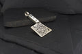 A silver axe-shaped pendant with intricate designs on a dark background.