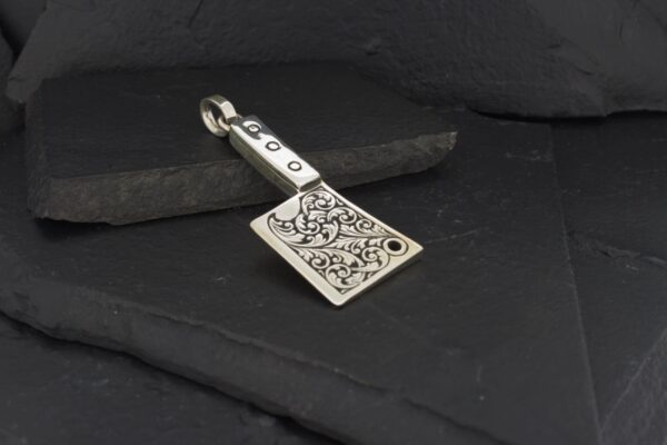 A silver axe-shaped pendant with intricate designs on a dark background.