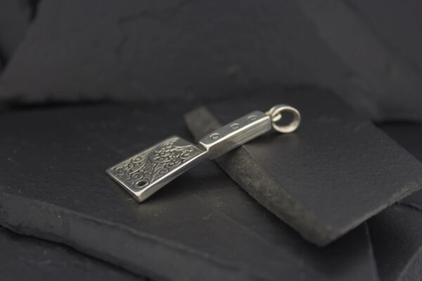 A silver pendant with intricate designs on a dark background.