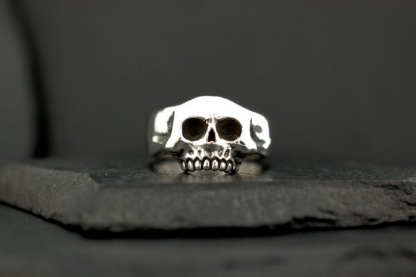 Close-up of a silver skull ring on a dark surface.