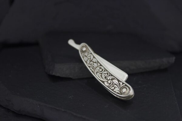 Intricately designed silver straight razor with floral patterns.