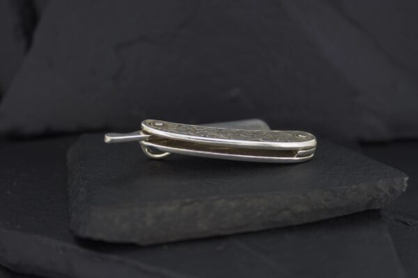 A folded pocket knife with a metallic handle on a dark surface.