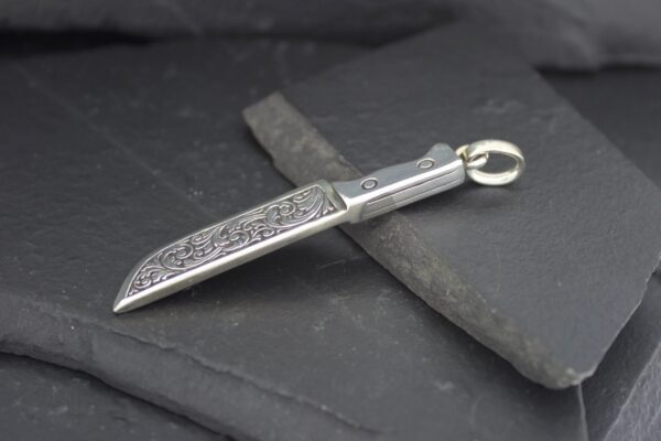 A silver pendant shaped like a detailed knife blade.