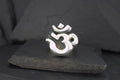 A silver Om symbol pendant on a dark surface.