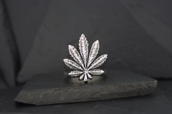 A silver cannabis leaf-shaped pendant on a dark surface.