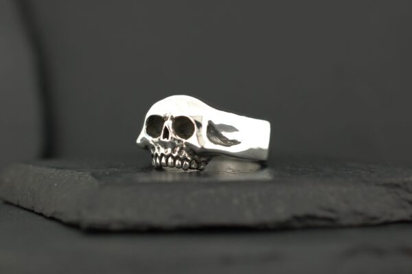 A silver skull-shaped ring on a dark surface.