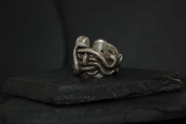 Intricate silver ring with a twisted knot design on a dark surface.