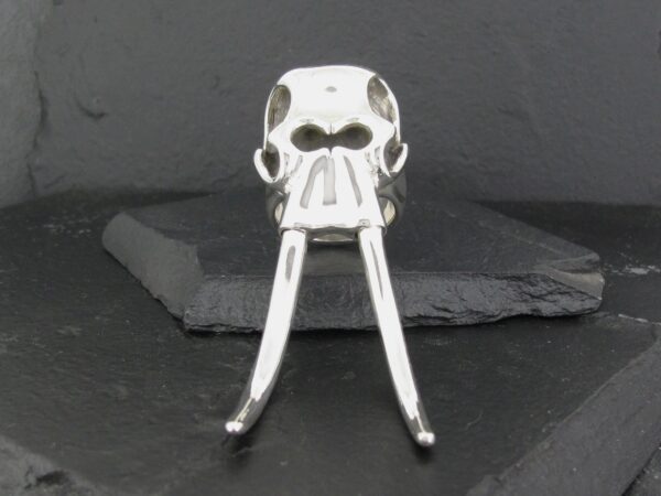 A metal skull-shaped bottle opener with long handles on a dark surface.