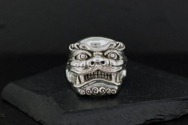 Intricately carved silver ring with a fierce mythical face design.