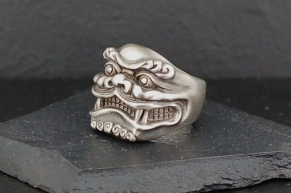 Intricately designed silver ring with a fierce mythical face.
