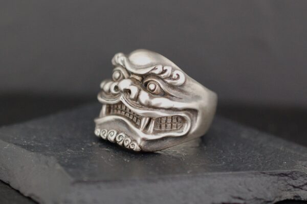 Intricately carved silver ring featuring a fierce mythical creature's face.