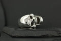 A polished silver skull ring with detailed features on a black background.