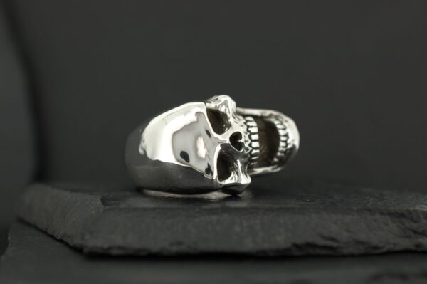 A polished silver skull ring with detailed features on a black background.