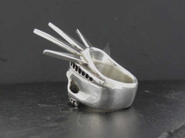 A silver ring designed like a mechanical skull with three prongs.