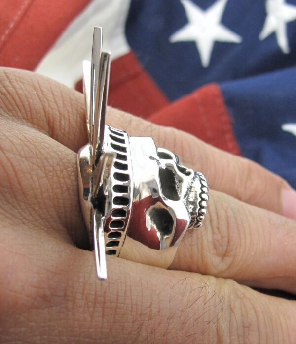A silver skull ring with a knife blade extending from the back, worn on a finger.