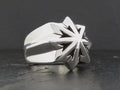 Silver ring with a sharp starburst design on a dark surface.