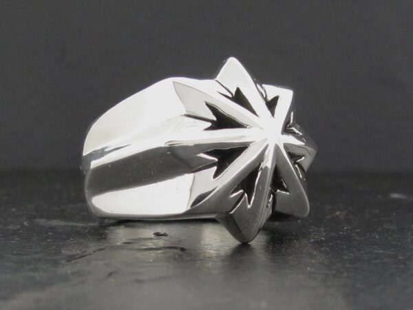 Silver ring with a sharp starburst design on a dark surface.