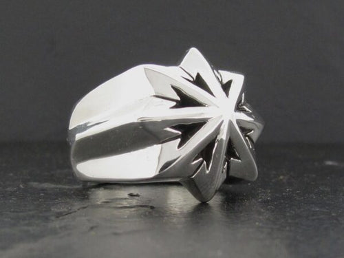 Silver ring with a sharp starburst design on a dark surface.