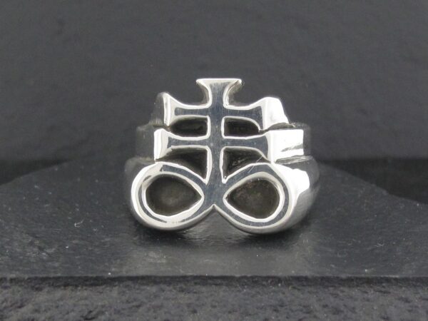 Silver ring with an intricate, symbolic design on a dark background.