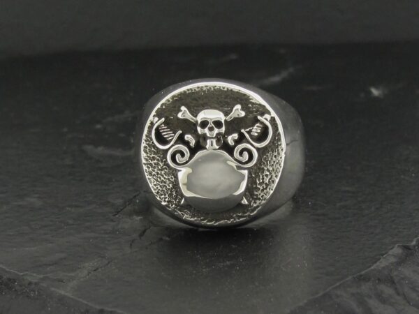 A silver ring with a skull and ornamental design on its face.