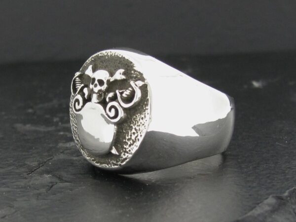 Silver ring with a skull design on a dark background.