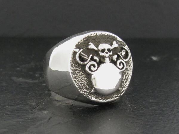 Silver skull ring with intricate designs on a dark surface.