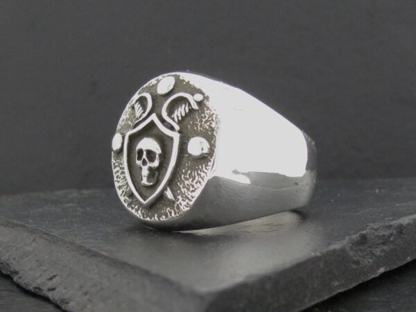 A silver ring with a skull and shield design.