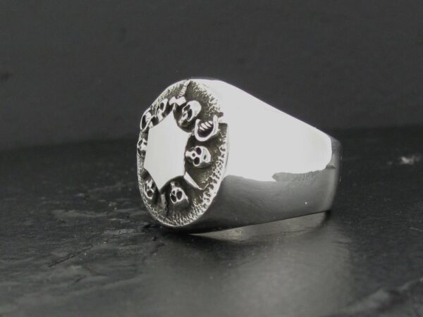 Silver ring with an ornate circular design on a dark background.