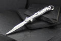 A sleek silver automatic knife with a pointed blade on dark slate stones.