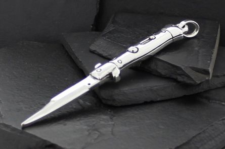 A sleek silver automatic knife with a pointed blade on dark slate stones.