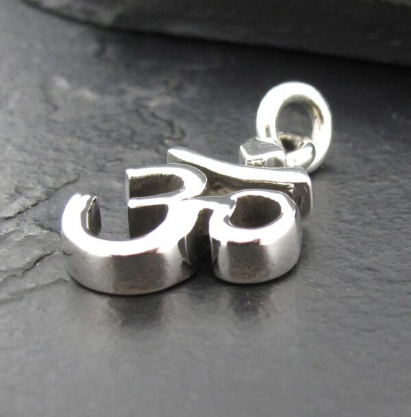Silver Om pendant resting on a dark textured surface.