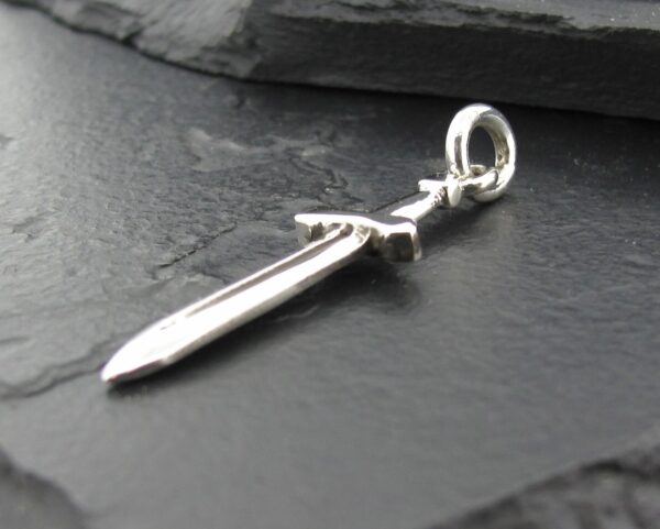 A silver sword pendant resting on a dark surface.