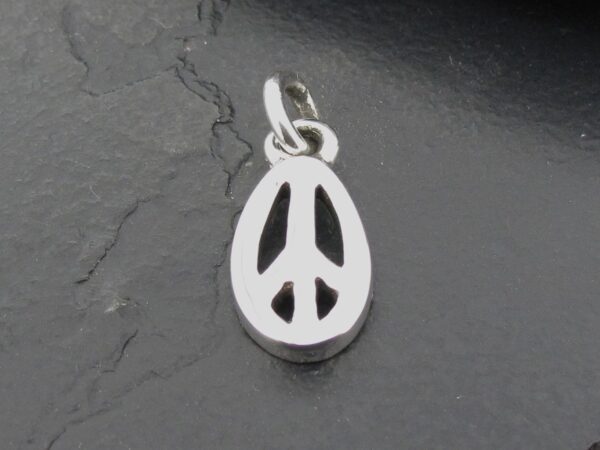 Silver peace sign pendant on a dark stone surface.