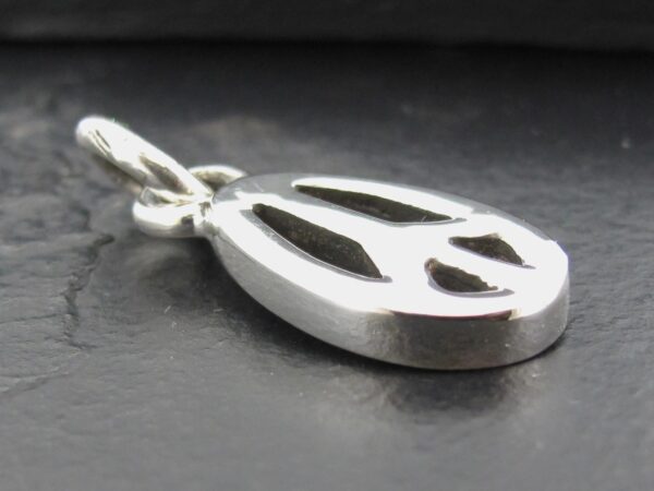 Close-up of a silver peace symbol pendant on a dark surface.