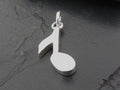 Silver pendant shaped like a musical note on a dark surface.