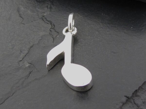 Silver pendant shaped like a musical note on a dark surface.