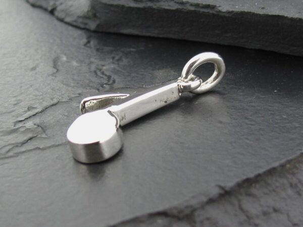 A small silver charm shaped like a ladle or spoon on a dark surface.