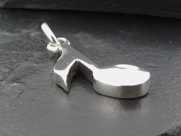 Close-up of a silver pendant shaped like a musical note on a dark surface.