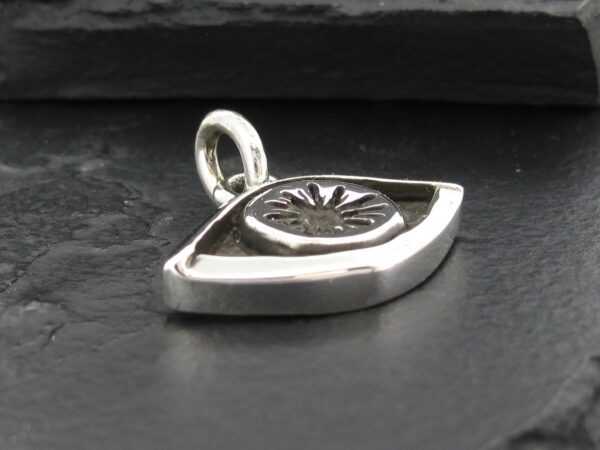 Silver eye-shaped pendant with intricate design on a dark surface.