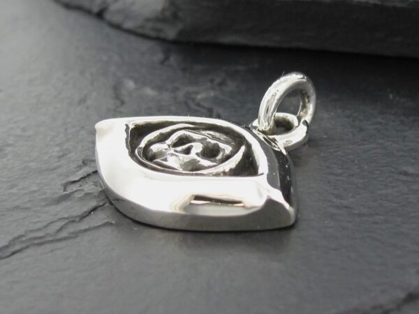 Close-up of a silver eye-shaped pendant on a dark surface.