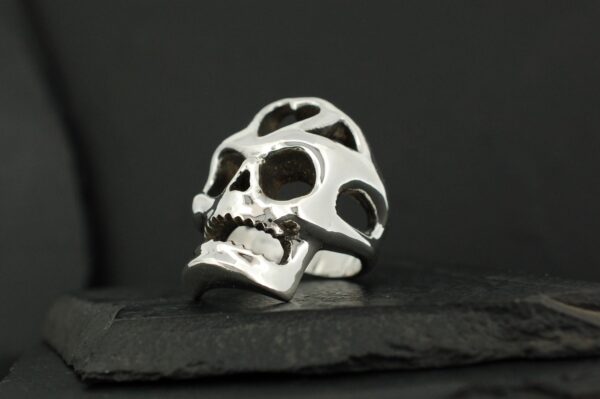 Silver skull ring with hollowed-out design on black background.